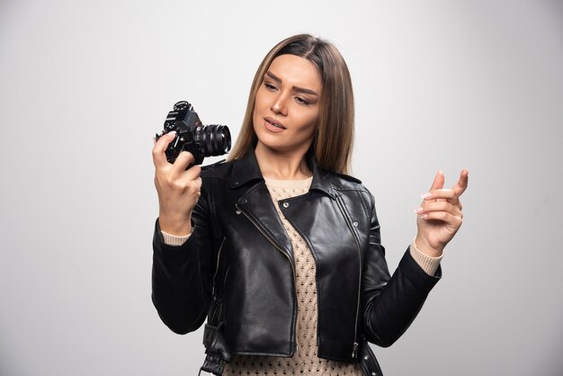 Blonde girl in black leather jacket checking her photo story at dslr and looks dissatisfied.