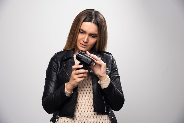 Blonde girl in black leather jacket checking her photo story at dslr and looks dissatisfied