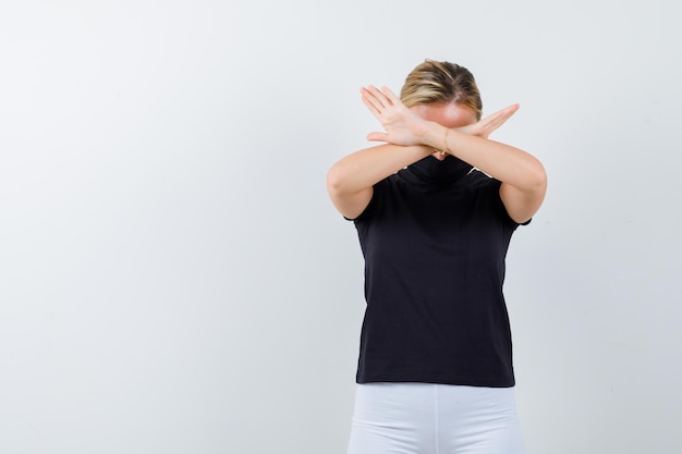 Blonde girl in black t-shirt, white pants, black mask holding arms crossed isolated