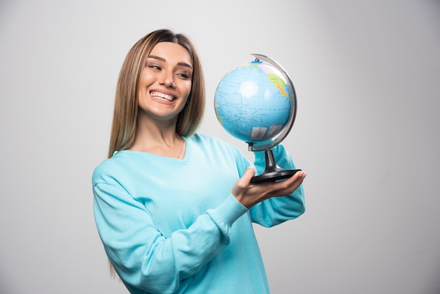 Blonde girl in blue sweatshirt holding a globe, guessing location and having fun.