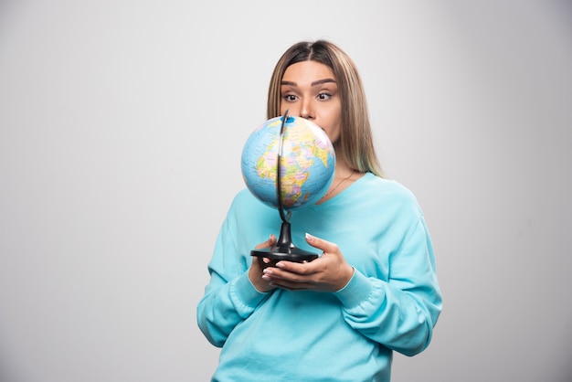 Blonde girl in blue sweatshirt holding a globe and looking surprized.
