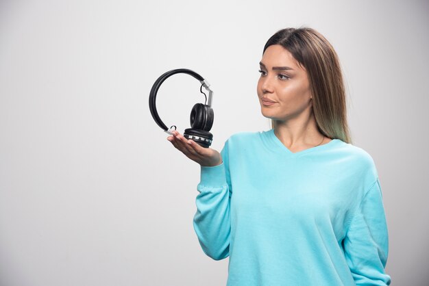 Blonde girl in blue sweatshirt holding headphones and gets ready to wear them to listen to the music.