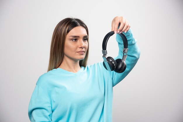 ヘッドフォンを保持し、音楽を聴くためにそれらを着用する準備ができて青いスウェットシャツのブロンドの女の子