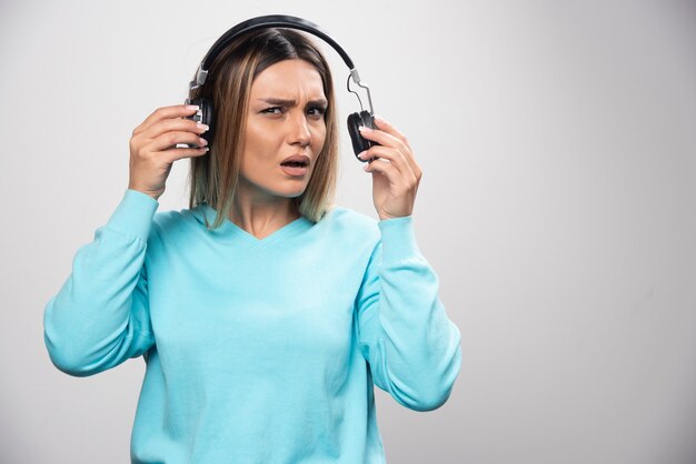 파란색 셔츠에 금발 소녀는 헤드폰을 듣고 음악을 즐기지 않습니다.