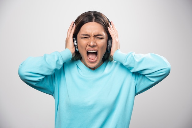 Blonde girl in blue sweatshirt listens the headphones and does not enjoy the music.