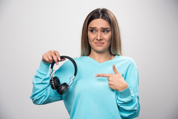 青いセーターのブロンドの女の子はヘッドフォンを聞いて音楽を楽しんでいません