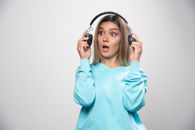 Blonde girl in blue sweatshirt taking out the headphones to hear the people around