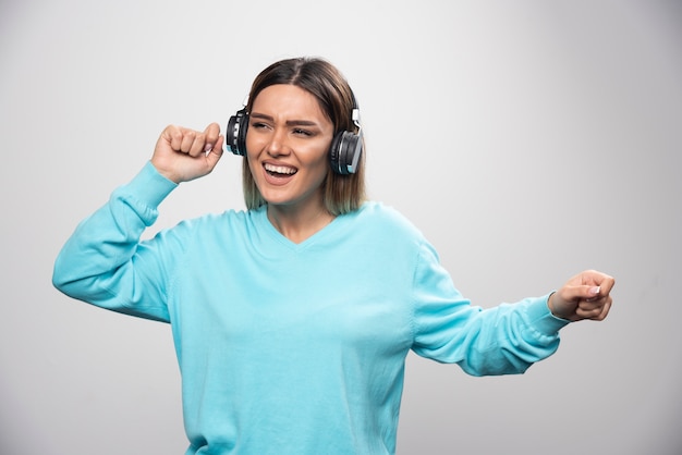 Blonde girl in blue sweatshirt wearing headphones, enjoying the music and having fun.