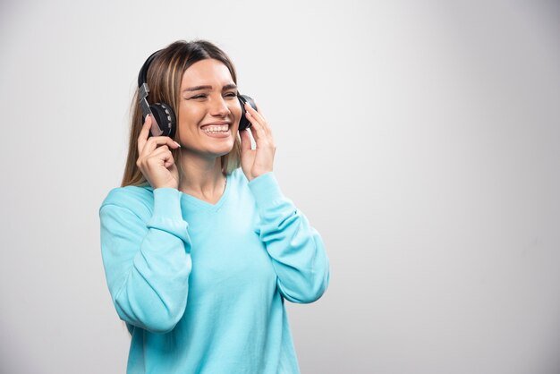 Blonde girl in blue sweatshirt wearing headphones, enjoying the music and having fun.