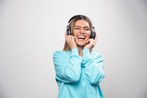 Ragazza bionda in felpa blu che indossa le cuffie, godersi la musica e divertirsi.