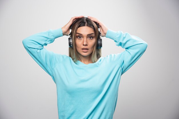 Blonde girl in blue sweatshirt wearing headphones, enjoying the music and having fun.