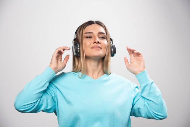 Blonde girl in blue sweatshirt wearing headphones, enjoying the music and having fun.