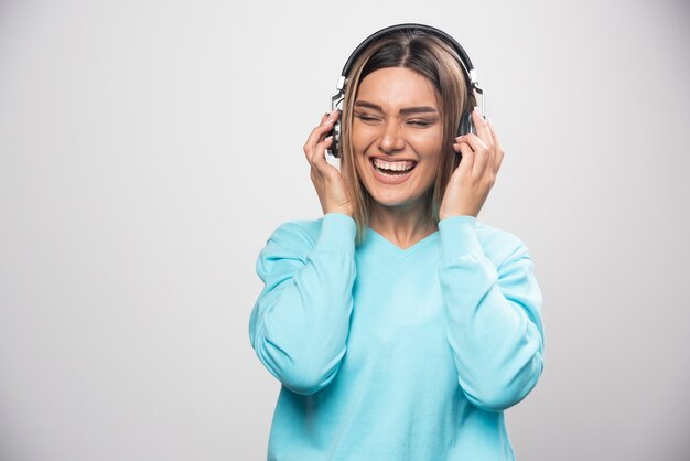 Blonde girl in blue sweatshirt wearing headphones, enjoying the music and having fun