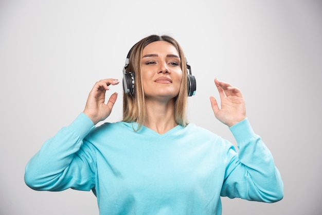 Blonde girl in blue sweatshirt wearing headphones, enjoying the music and having fun