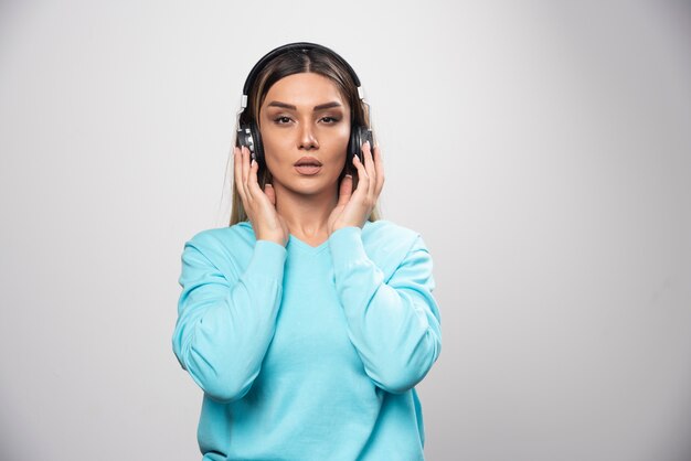 Blonde girl in blue sweatshirt wearing headphones and trying to understand the music.