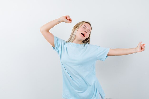 青いTシャツのストレッチとあくび、目を閉じて眠そうな顔をした金髪の少女、正面図。