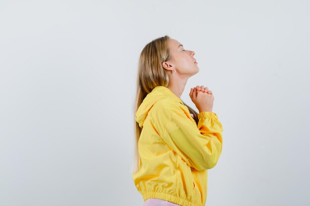 Blonde girl clasping hands in praying gesture in t-shirt, jacket and looking hopeful. .