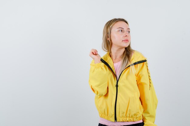 금발 소녀 주먹을 움켜 쥐고 분홍색 티셔츠와 노란색 재킷을 입고 매혹적인 찾고