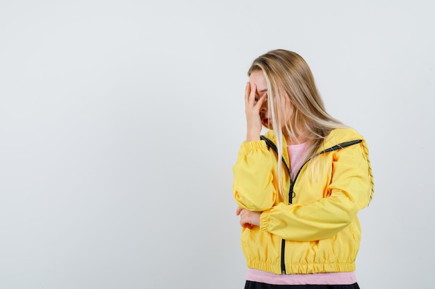 Бесплатное фото Блондинка закрыла лицо рукой в розовой футболке и желтой куртке и выглядела раздраженной