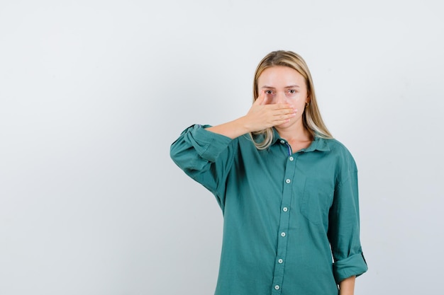 Blonde girl covering mouth with hand in green blouse and looking serious