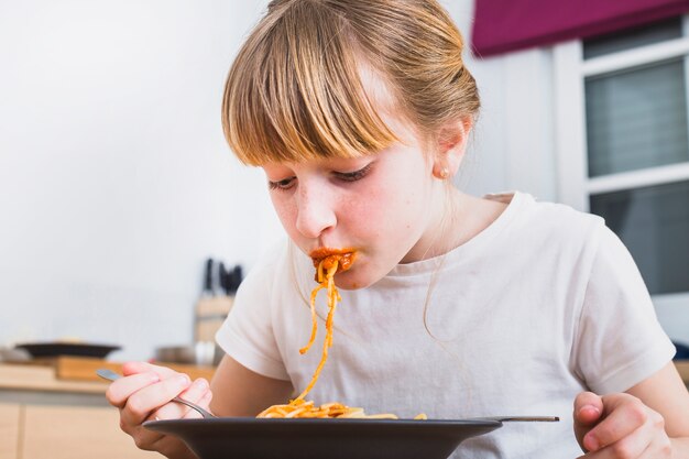 Blonde girl eating pasta in kitchen