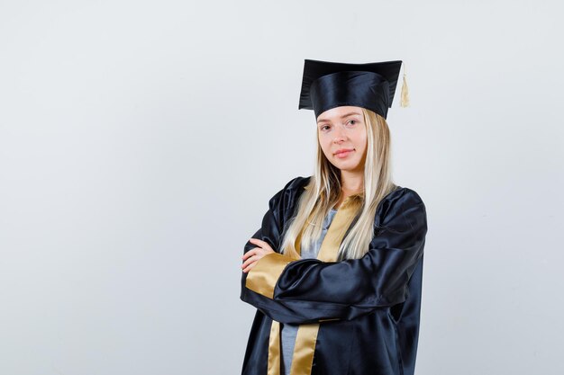 Blonde girl in graduation gown and cap standing arms crossed and looking confident
