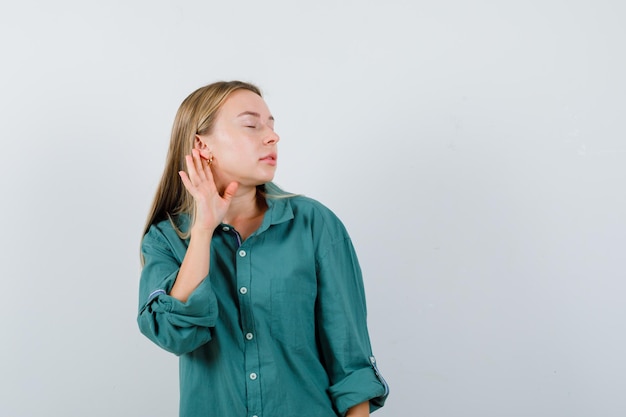 Blonde girl in green blouse holding hand near ear to hear something and looking focused