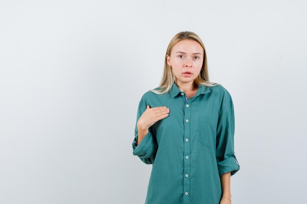 Blonde girl in green blouse pointing herself and looking enchanting