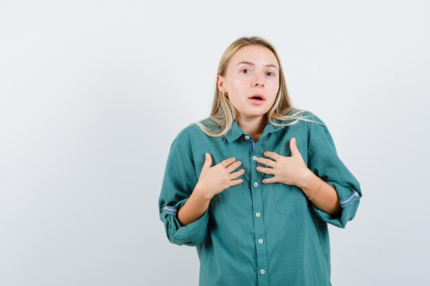 Blonde girl in green blouse pointing herself and looking excited