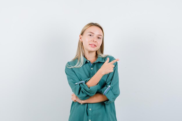 Blonde girl in green blouse pointing right with index finger and looking pretty