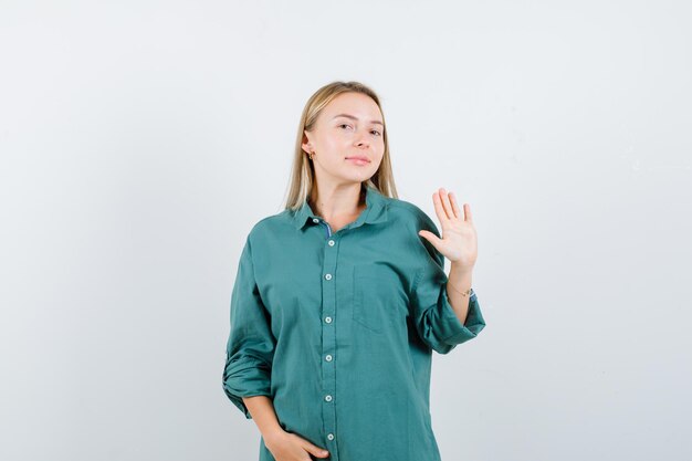 Blonde girl in green blouse showing stop sign while holding hand on belly and looking pretty