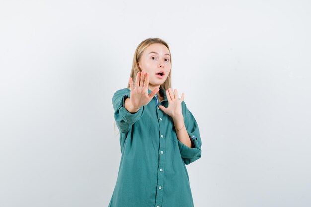 Blonde girl in green blouse showing stop signs and looking surprised