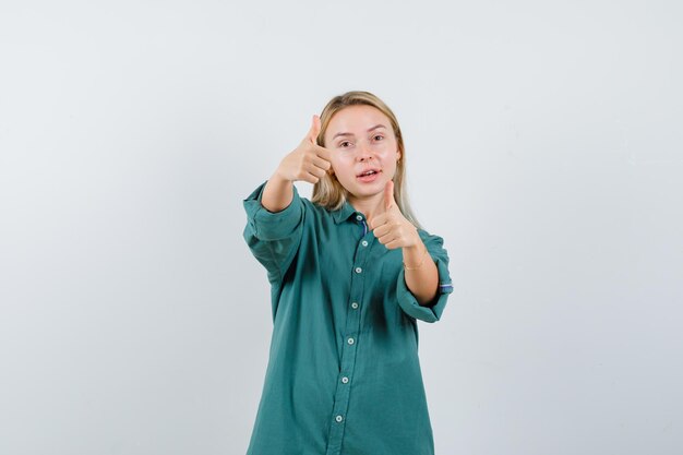 Blonde girl in green blouse showing thumbs up with both hands and looking pretty