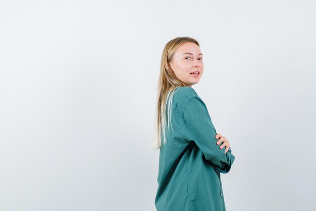 Blonde girl in green blouse standing arms crossed, looking over shoulder and looking pretty