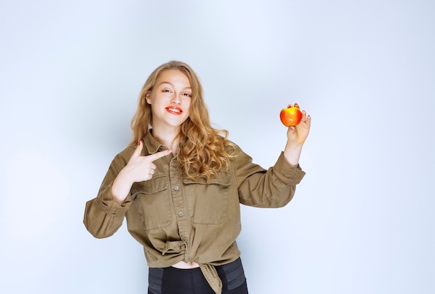 Бесплатное фото Белокурая девочка держит и продвигает красный персик.
