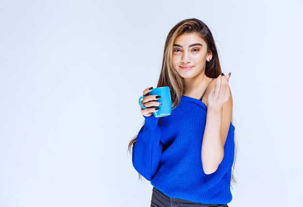 Белокурая девушка держит голубую кофейную кружку.