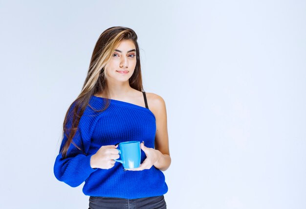 Белокурая девушка держит голубую кофейную кружку.
