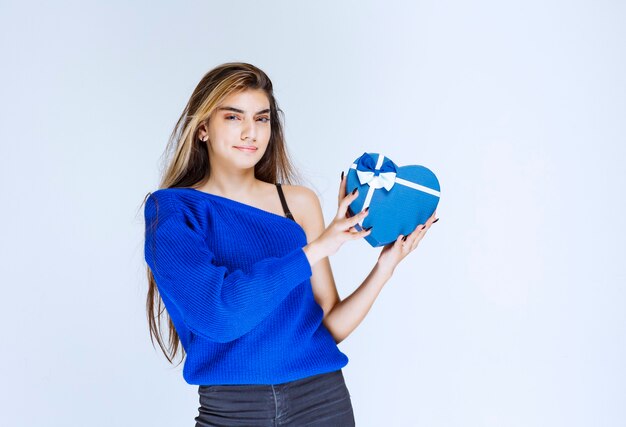 Blonde girl holding a blue heart shape gift box.