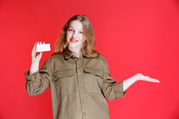 Blonde girl holding a business card and pointing at her colleague.