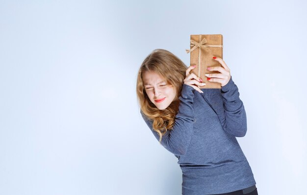 Blonde girl holding a cardboard gift box and looks confused and thoughtful. 