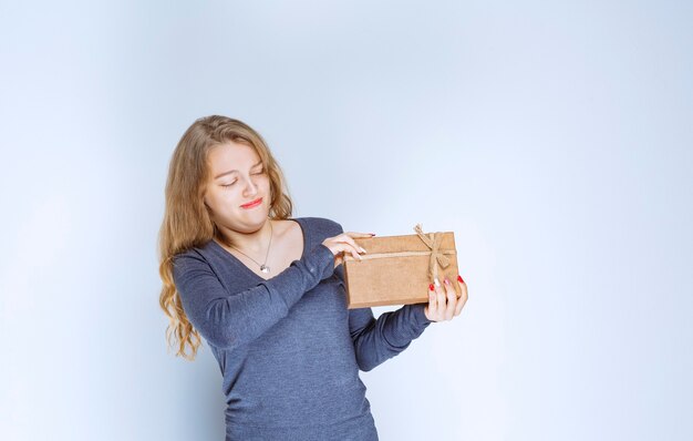 Blonde girl holding a cardboard gift box and looks confused and thoughtful.