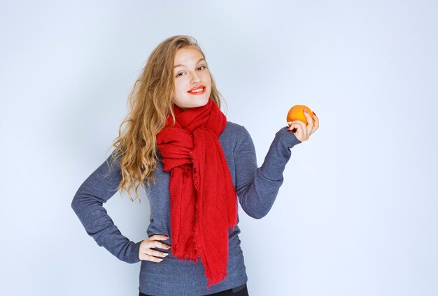 オレンジ色の果物を保持し、デモンストレーションするブロンドの女の子。