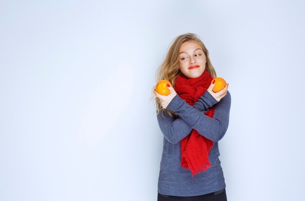 Blonde girl holding and demonstrating orange fruits.