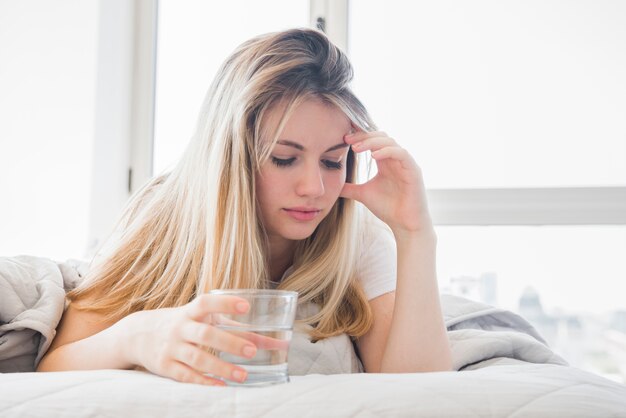 Blonde girl holding glass of water on the bed