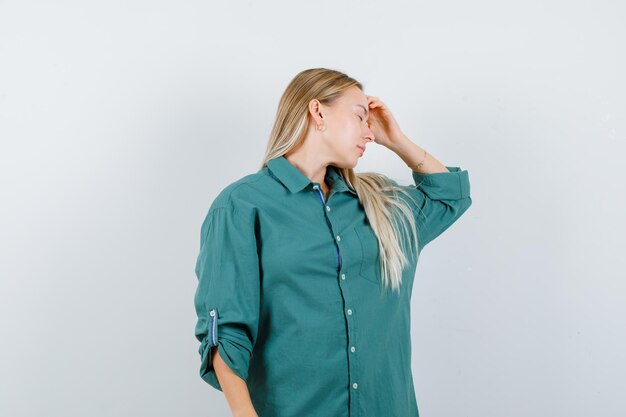 Blonde girl holding hand on forehead, having headache in green blouse and looking annoyed.