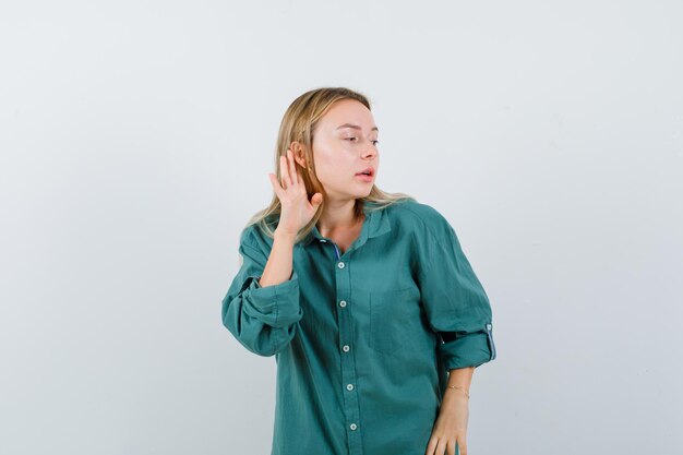 Blonde girl holding hand near ear to hear something in green blouse and looking focused