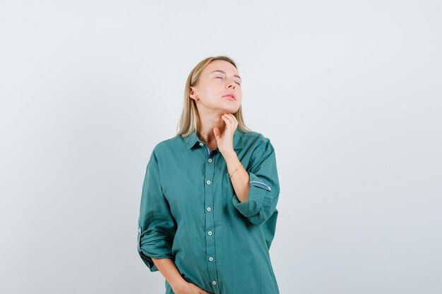 Blonde girl holding hand on neck, closing eyes in green blouse and looking calm