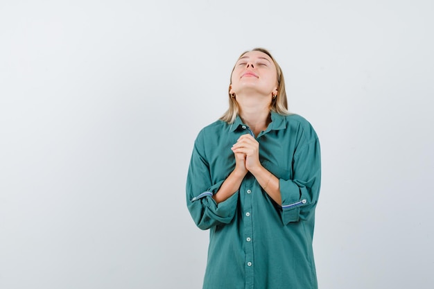 Free photo blonde girl holding hands clasped, praying in green blouse and looking focused