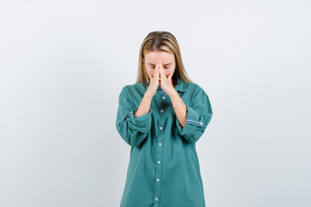 Ragazza bionda che si tiene per mano stretta, pregando in camicetta verde e guardando concentrata