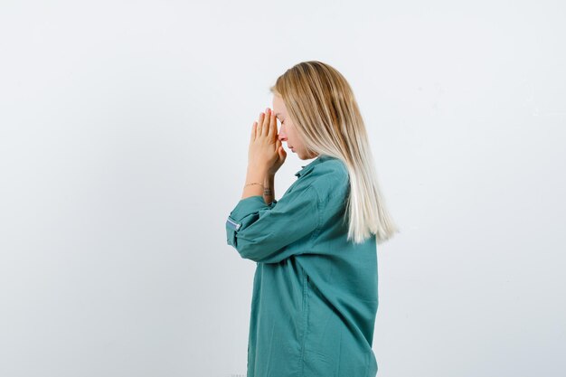 Blonde girl holding hands clasped, praying in green blouse and looking focused